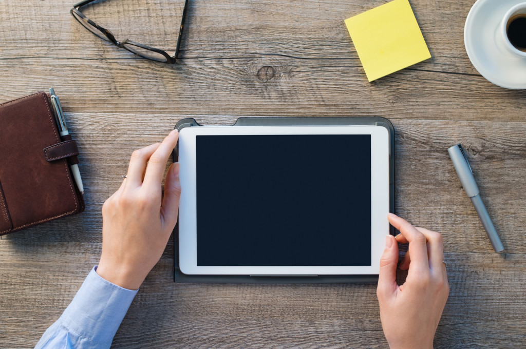 Closeup shot of a woman hands holding digital tablet. Businesswoman is holding a palmtop on desk at office. Blank scrren to put it on your own design